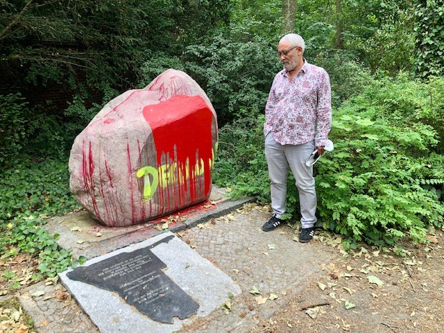 Ein Mann steht neben dem Stein mit Inschrift, der mit roter Farbe beschmiert ist.