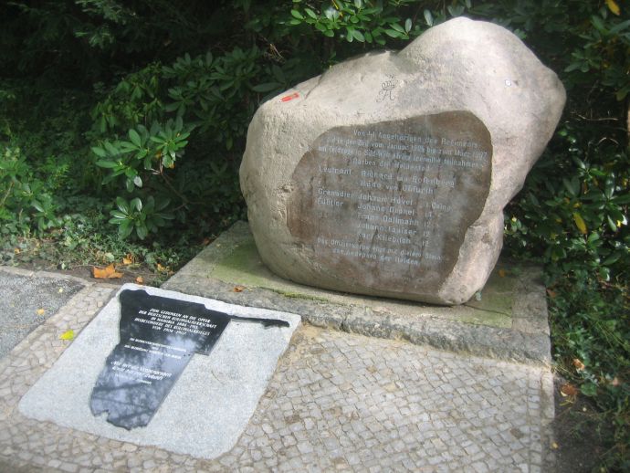 Ein Stein mit Inschrift, dvor in den Boden eingelassen eine glänzende Platte mit Inschrift in der Form des Landes Namibia,