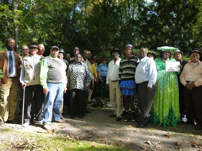 Gruppe Schwarzer Menschen steht zusammen, so, dass nur die schwarze Platte im Boden zu sehen ist.