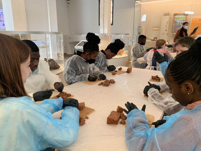 eine Gruppe Schüler:innen sitzt an einem Tisch und arbeitet mit Ton.