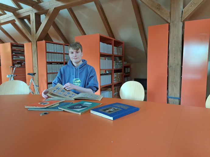 Timo im Geschichtsspeicher. Foto: Museum Neukölln Timo sitzt am Tisch im Geschichtsspeicher. Er blättert in einem historischen Sammelalbum.