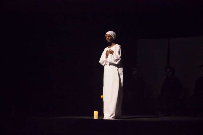 Ein Mann in weißer Kleidung vor schwarzem Hintergrund.