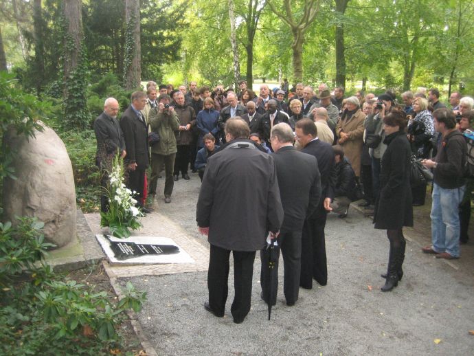 große Menschenmenge um einen Stein und eine in den Boden eingelassene schwarze Platte. vor dem Stein 