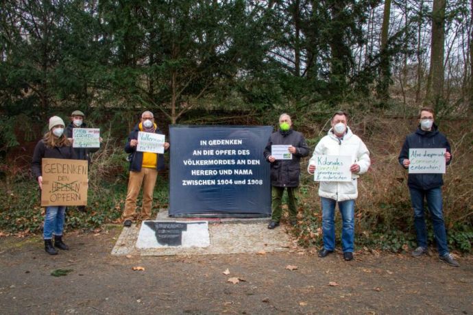 6 Menschen stehen um den schwarzen Kasten herum und halten Plakate hoch.