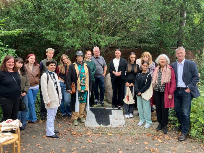 Gruppenfoto: die Schüler:_innen der AEO, Gruppeleiter Michael Küppers-Adebisi und Museumslehrerin Silvia Haslauer, Museumsleiter Dr. Henkel und  Bezirkstaträtin Wolter (Foto: FB MSE 2025) Gruppenfoto, 15 Leute unterschieldichen Atlers und Geschlechts stehen um den sog. Hereo-Stein herum.