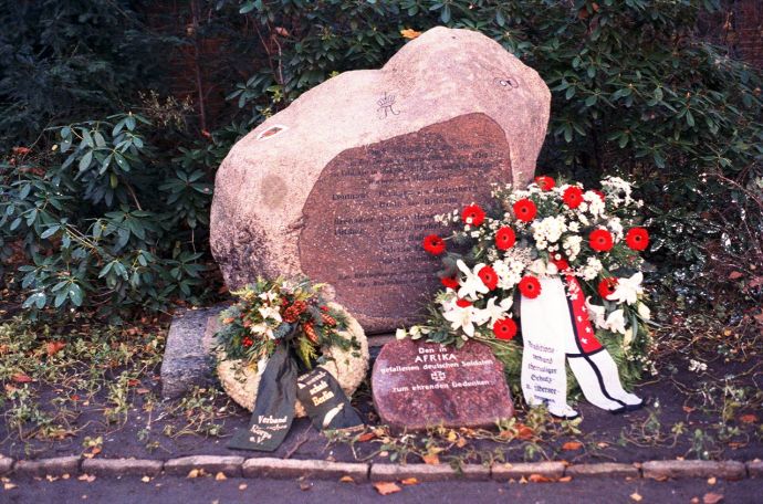 Zwei Steine mit Inschrift, drumherum sind Blumenkränze drapiert.