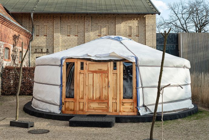 Zu sehen ist eine Jurte: Ein rundes, weißes Zelt, das eine Holztür hat.