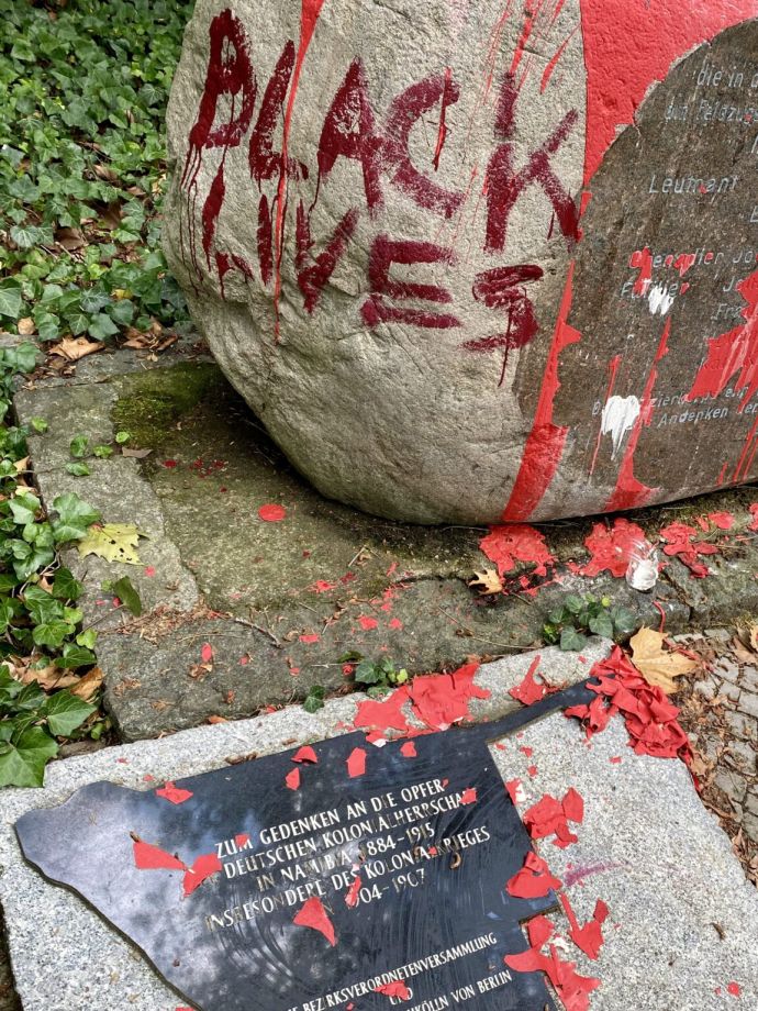 Nahaufnahme des Steins und der Gedenkplatte, die mit roter Farbe beschmiert wurden. Auf dem Stein steht in rot: Black Lives Matter